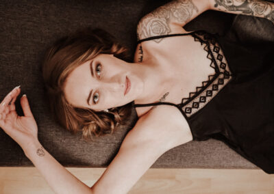 Sinnliche Boudoir-Fotografie im Hotelzimmer mit hübscher Frau in schwarzer Unterwäsche auf dem Boden.